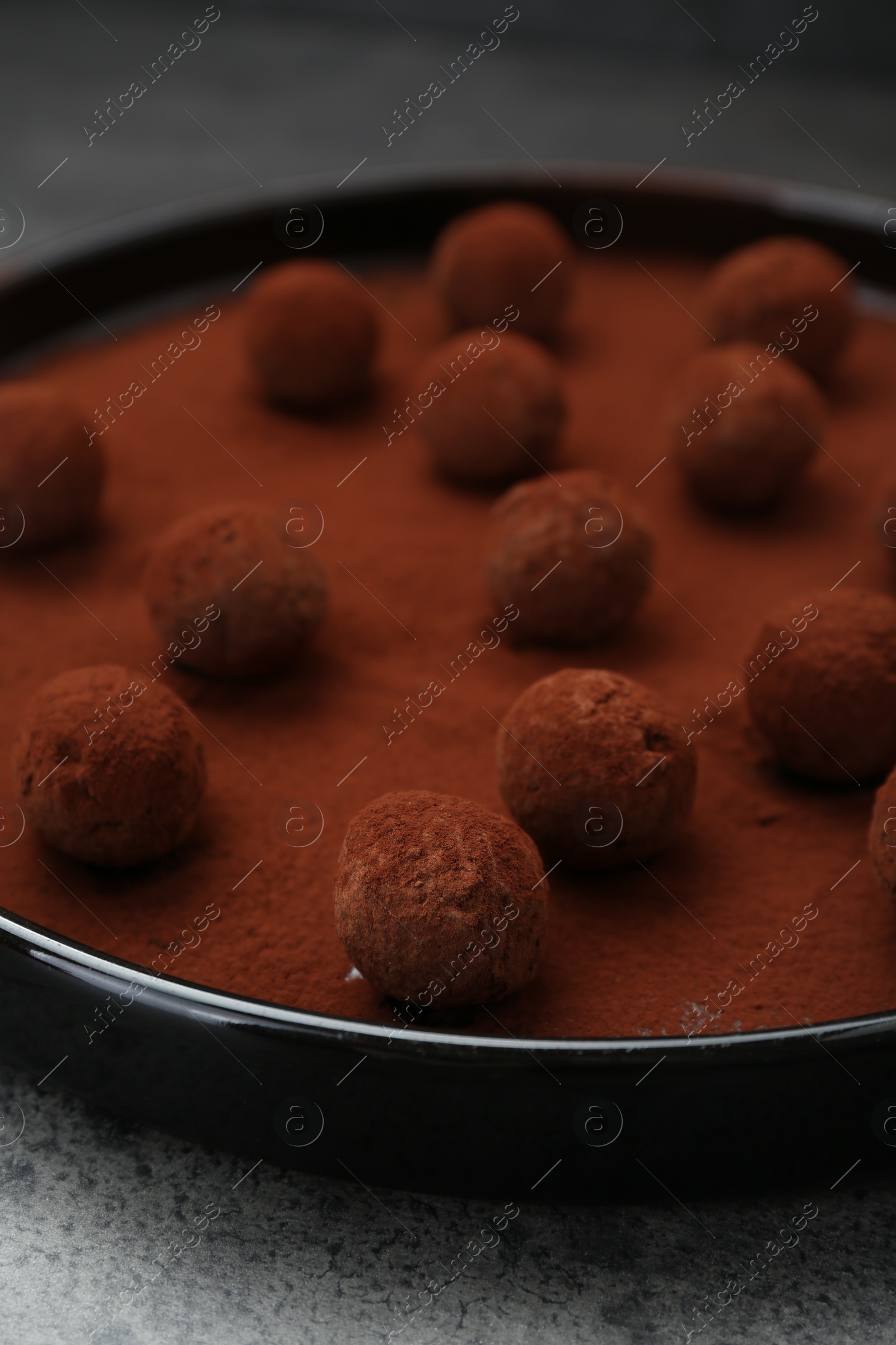 Photo of Delicious chocolate candies powdered with cocoa on grey table, closeup