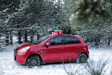 Photo of Car with Christmas tree and gifts in snowy forest on winter day