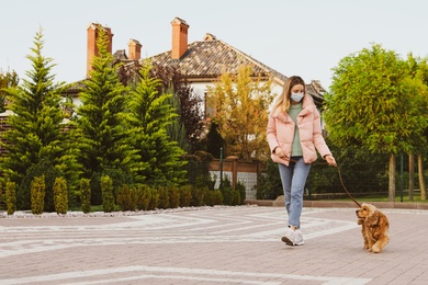 Woman in protective mask with English Cocker Spaniel outdoors. Walking dog during COVID-19 pandemic