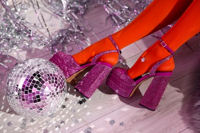 Woman in orange tights and pink high heeled shoes near disco ball indoors, above view