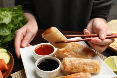 Woman eating tasty fried spring rolls at table, closeup