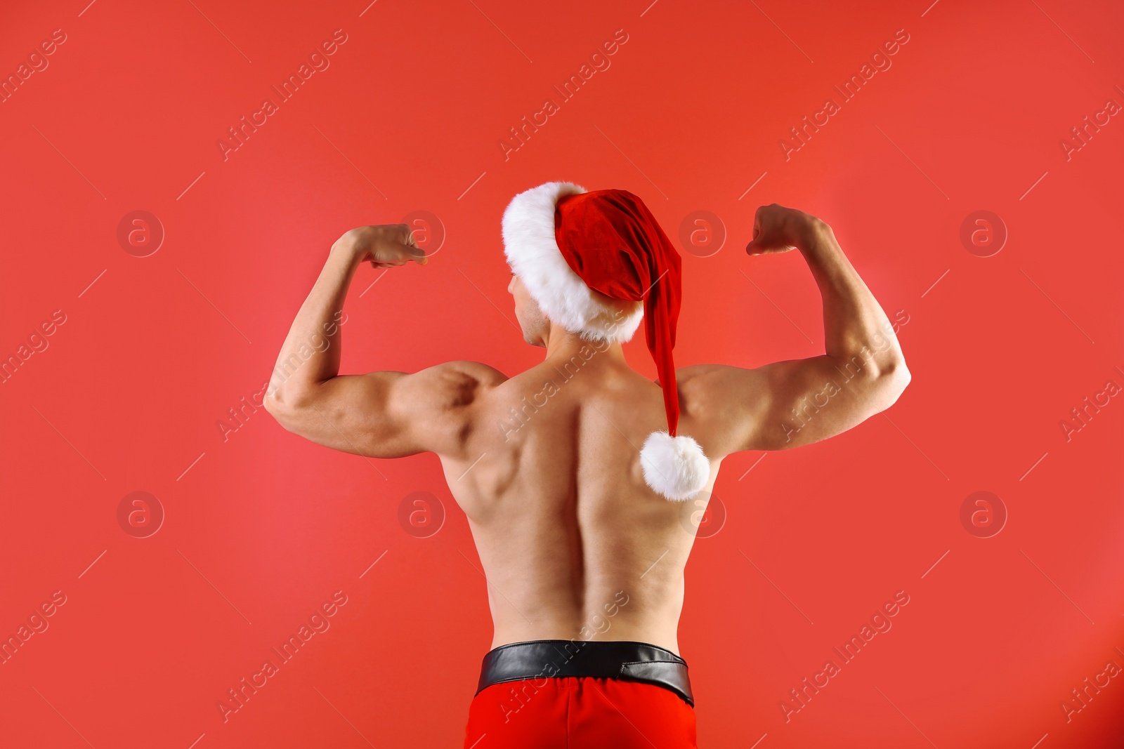 Photo of Young muscular man in Santa hat on color background