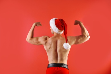 Photo of Young muscular man in Santa hat on color background