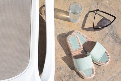 Stylish slippers, sunglasses, glass of water and grey sunbed outdoors. Beach accessories
