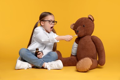 Little girl playing doctor with toy bear on yellow background