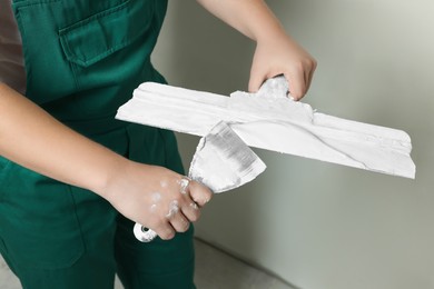 Photo of Professional worker holding putty knives with plaster indoors, closeup
