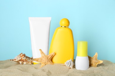 Photo of Different suntan products, seashell and starfishes on sand against light blue background