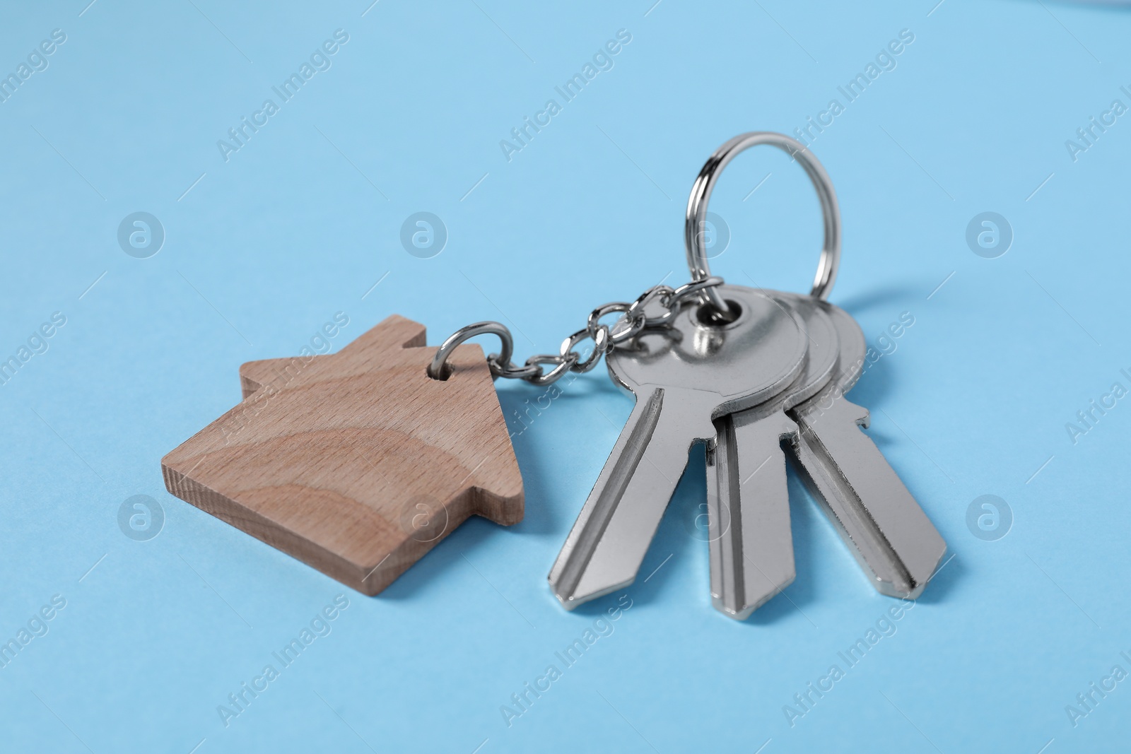 Photo of Keys with keychain in shape of house on light blue background, closeup