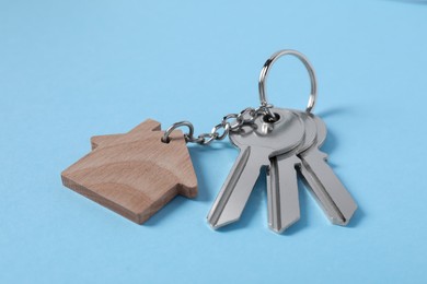 Photo of Keys with keychain in shape of house on light blue background, closeup