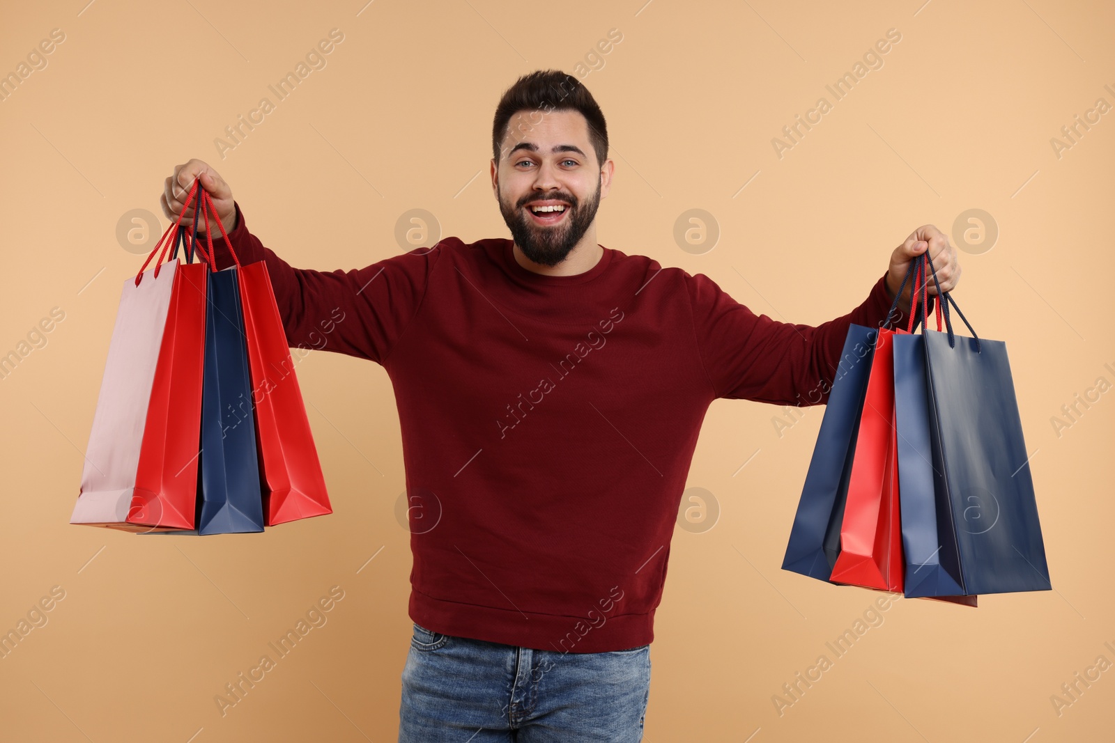 Photo of Happy man with many paper shopping bags on beige background