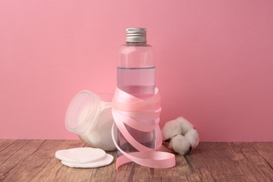 Photo of Composition with makeup remover and cotton flower on wooden table against pink background
