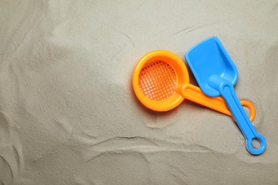 Photo of Plastic toy shovel and sieve on sand, flat lay