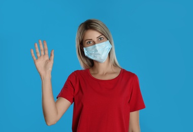 Photo of Woman in protective mask showing hello gesture on light blue background. Keeping social distance during coronavirus pandemic