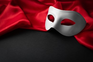 Photo of White theatre mask and red fabric on black background. Space for text