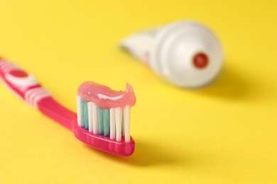 Photo of Pink brush with toothpaste on yellow background, closeup. Space for text