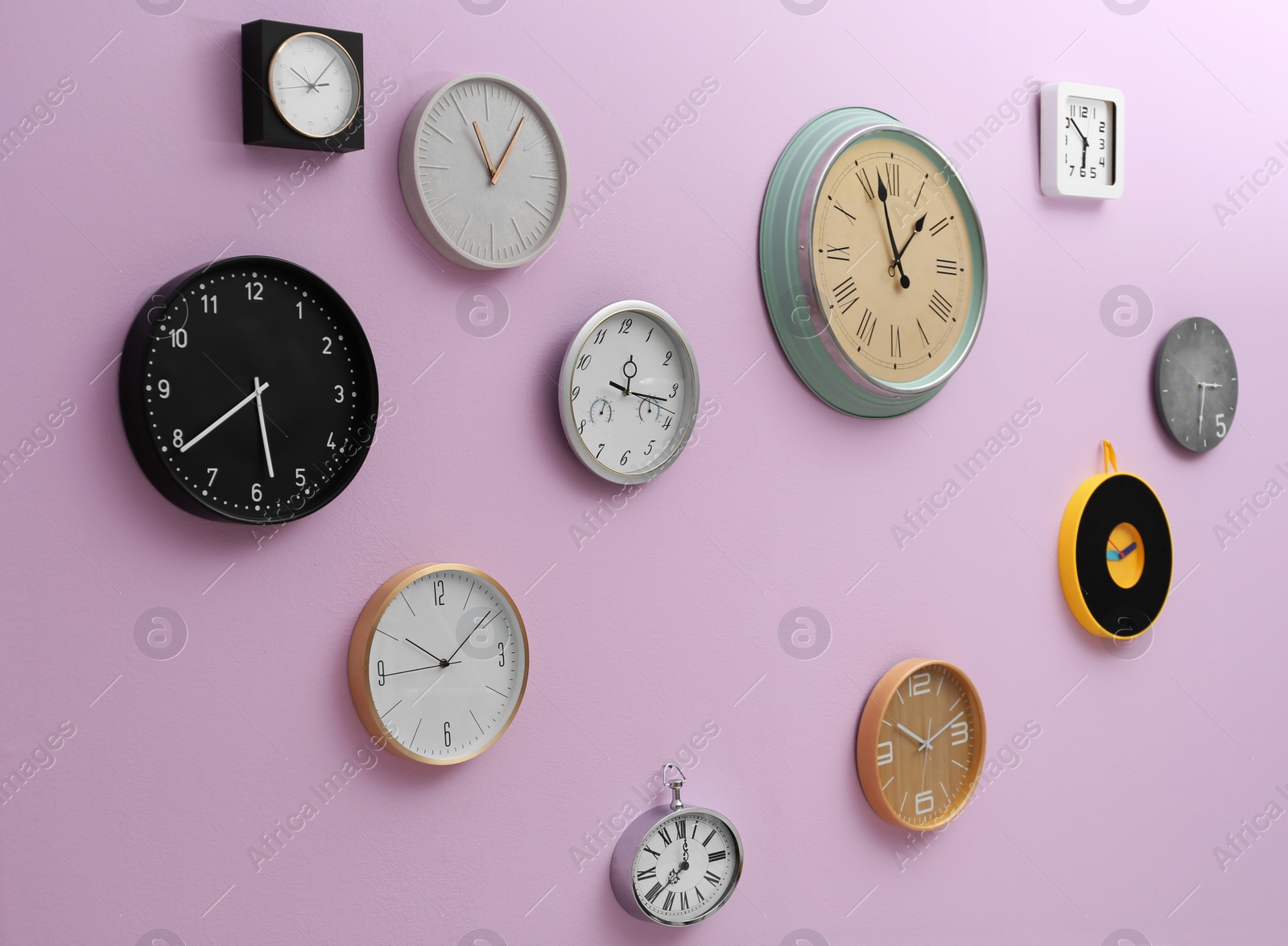 Photo of Many different clocks hanging on color wall. Time of day