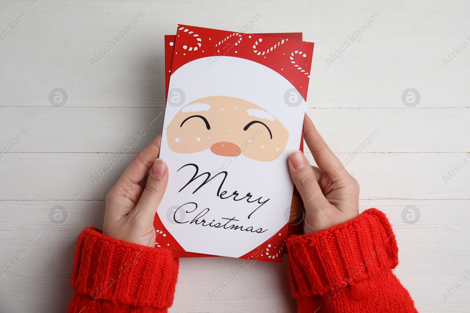 Photo of Woman holding Christmas cards at white wooden table, top view