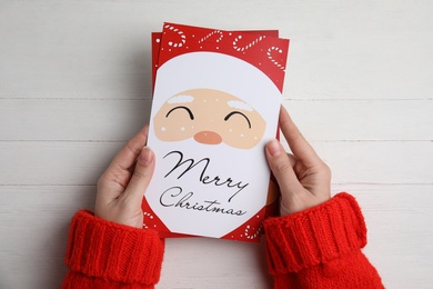 Photo of Woman holding Christmas cards at white wooden table, top view