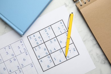 Photo of Sudoku, pen, planner and notepad on white marble table, flat lay