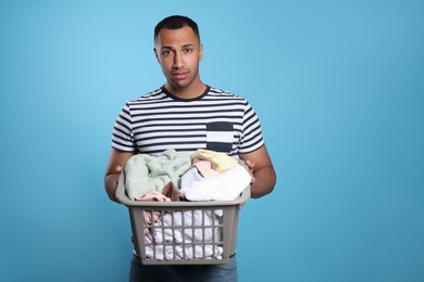 Photo of Young man with basket full of laundry on light blue background