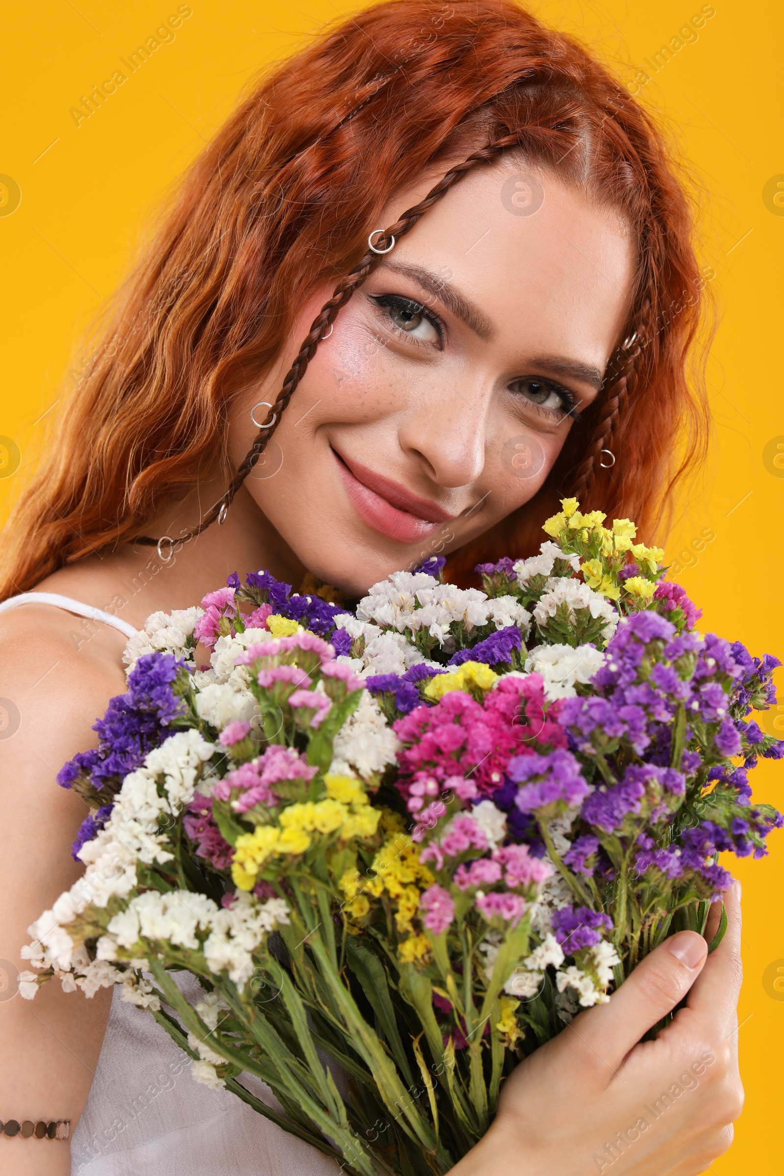 Photo of Beautiful young hippie woman with bouquet of colorful flowers on orange background, closeup