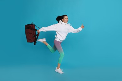 Photo of Beautiful woman with sports bag running on light blue background