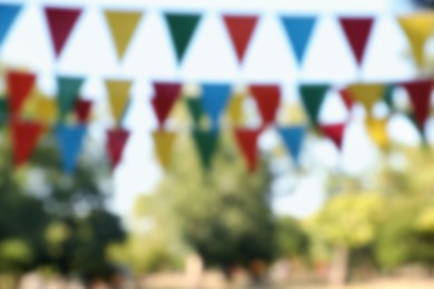Blurred view of colorful bunting flags in park. Party decor
