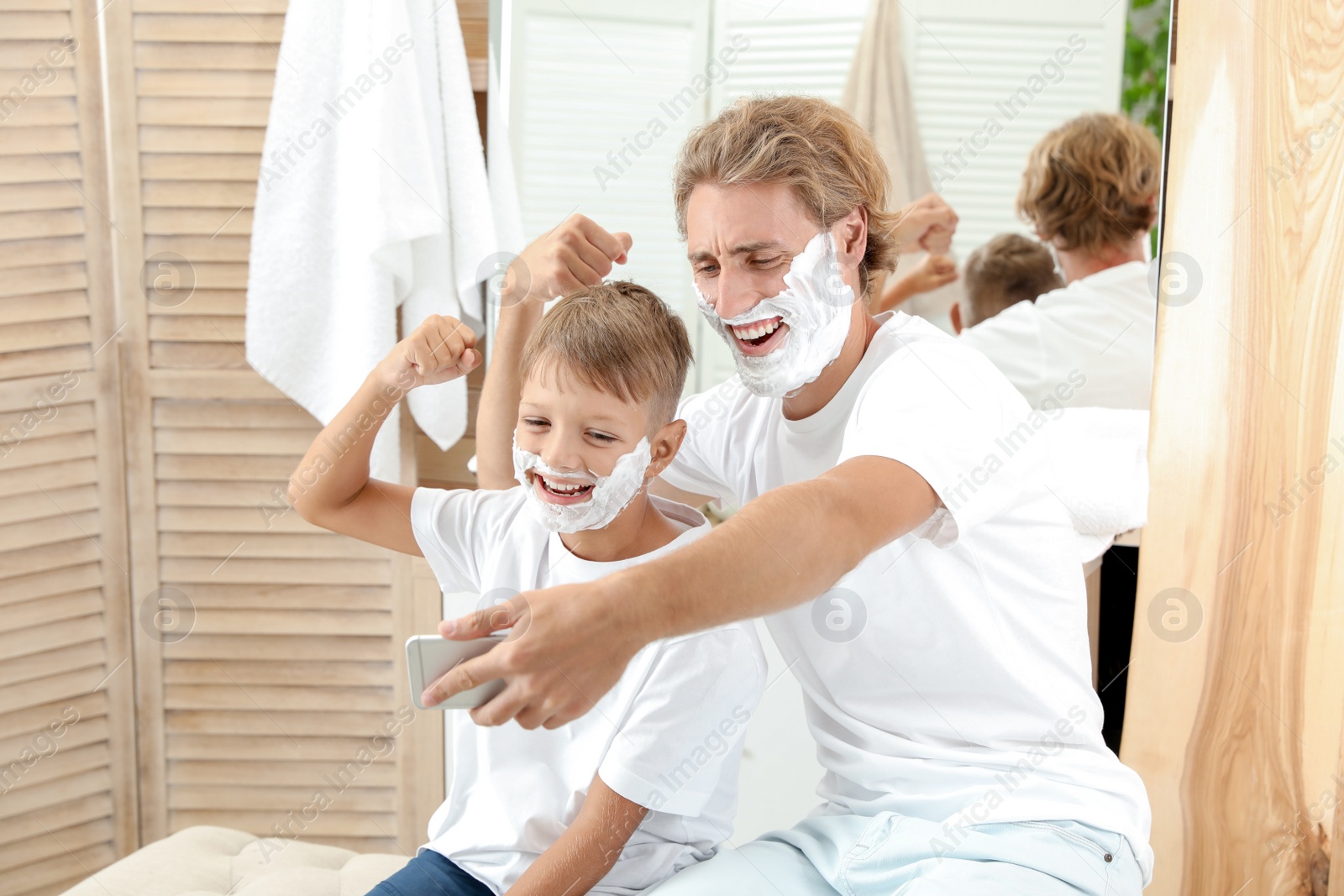 Photo of Father and son taking selfie with shaving foam on faces in bathroom