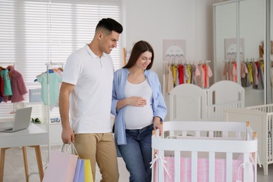 Photo of Happy pregnant woman and her husband with shopping bags choosing crib in store