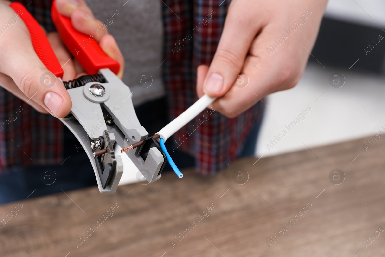 Photo of Professional electrician stripping wiring at wooden table, closeup