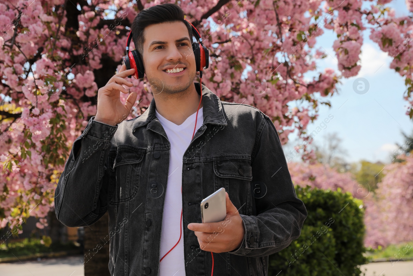 Photo of Happy man with smartphone listening to audiobook outdoors on spring day