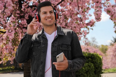 Happy man with smartphone listening to audiobook outdoors on spring day