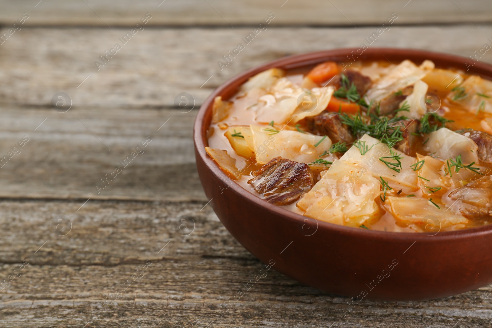 Photo of Tasty cabbage soup with meat, carrot and dill on wooden table, closeup. Space for text