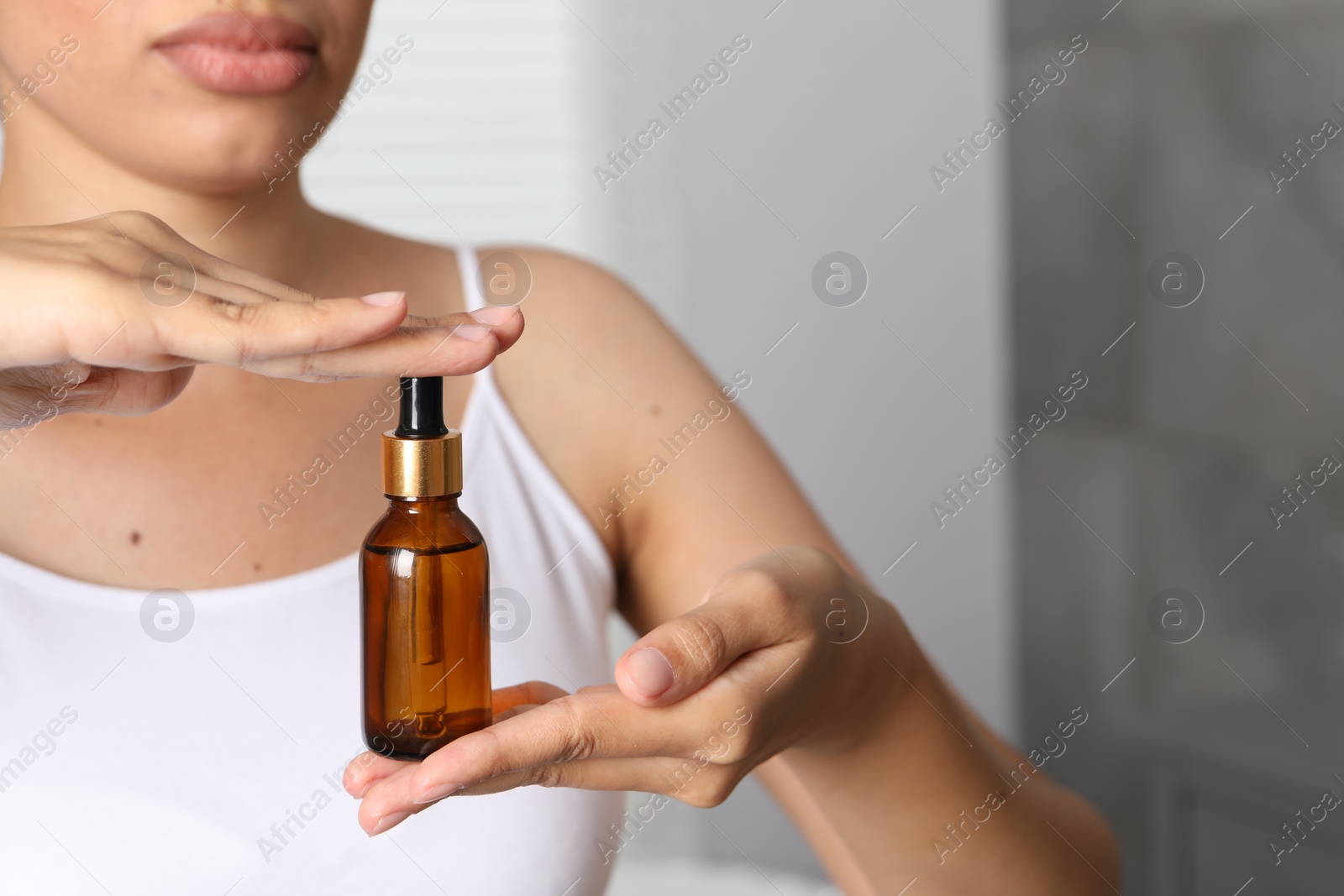 Photo of Woman with bottle of cosmetic serum on blurred background, closeup. Space for text