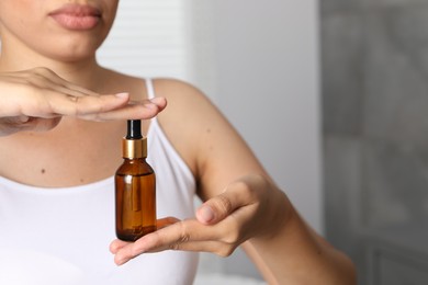 Photo of Woman with bottle of cosmetic serum on blurred background, closeup. Space for text