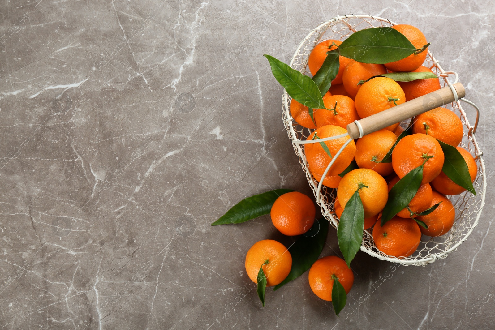 Photo of Fresh tangerines with green leaves on grey table, flat lay. Space for text