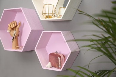 Photo of Hexagon shaped shelves with different stuff on grey wall. Interior design