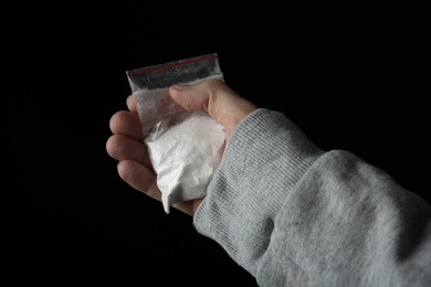 Drug dealer holding bag with cocaine on black background, closeup