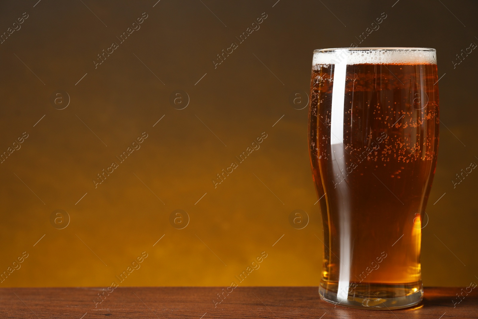 Photo of Glass with fresh beer on wooden table against dark background. Space for text