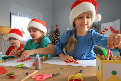 Photo of Cute little children in Santa hats making beautiful Christmas greeting cards at home