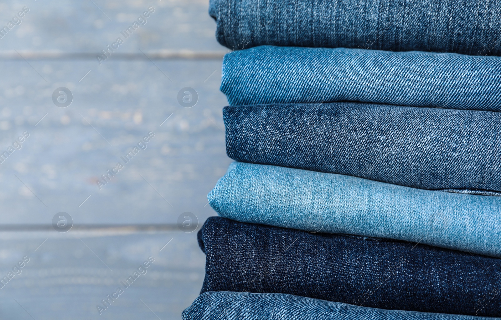 Photo of Stack of different jeans on grey wooden background, closeup