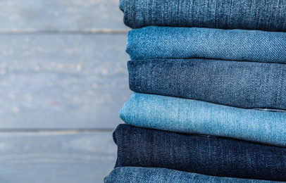 Stack of different jeans on grey wooden background, closeup