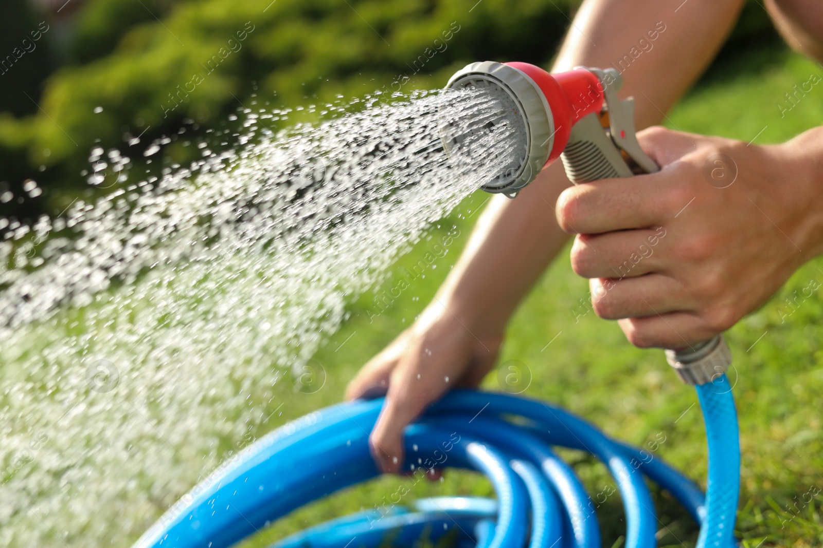 Photo of Man spraying water from hose in garden, closeup