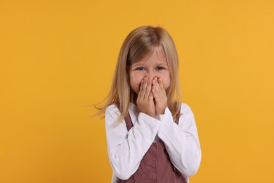 Photo of Embarrassed little girl covering mouth with hands on orange background
