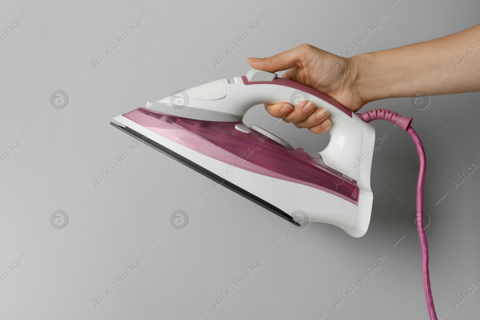 Photo of Woman holding modern iron on light grey background, closeup