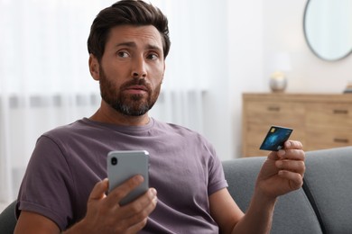 Man with credit card using smartphone on sofa at home. Be careful - fraud