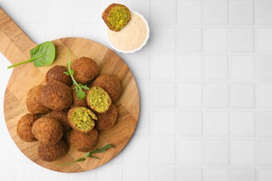 Delicious falafel balls, herbs and sauce on white tiled table, top view. Space for text