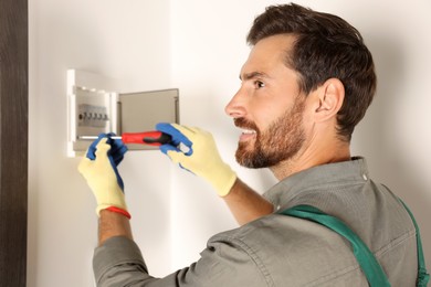 Photo of Electrician installing fuse box with screwdriver indoors