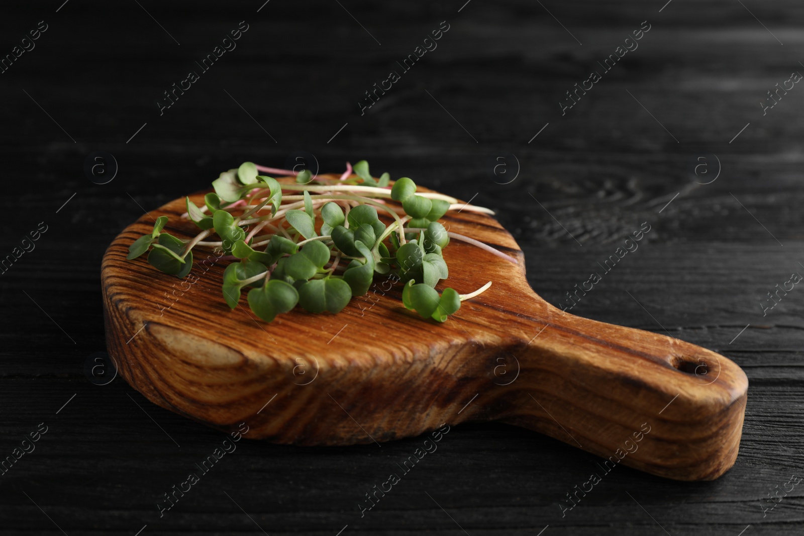 Photo of Board with cut fresh radish microgreens on black wooden table