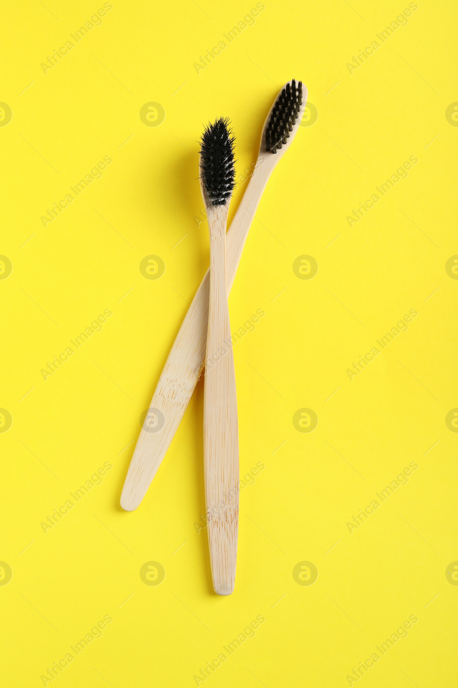 Photo of Two bamboo toothbrushes on yellow background, flat lay
